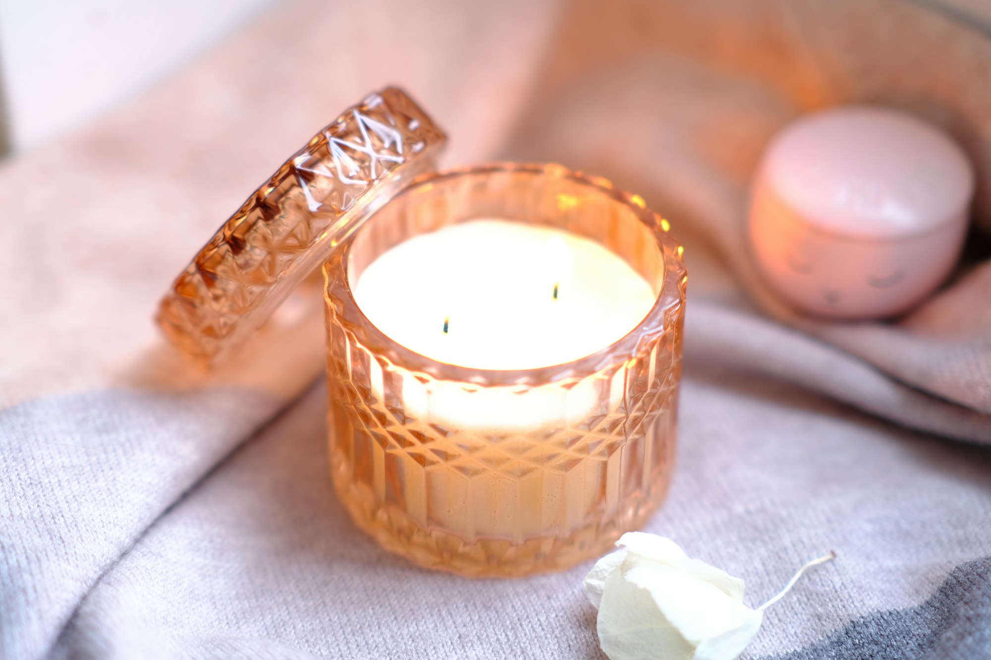 A big beautiful neutral light pink candle in a glass candlestick with dry flower on a textile.